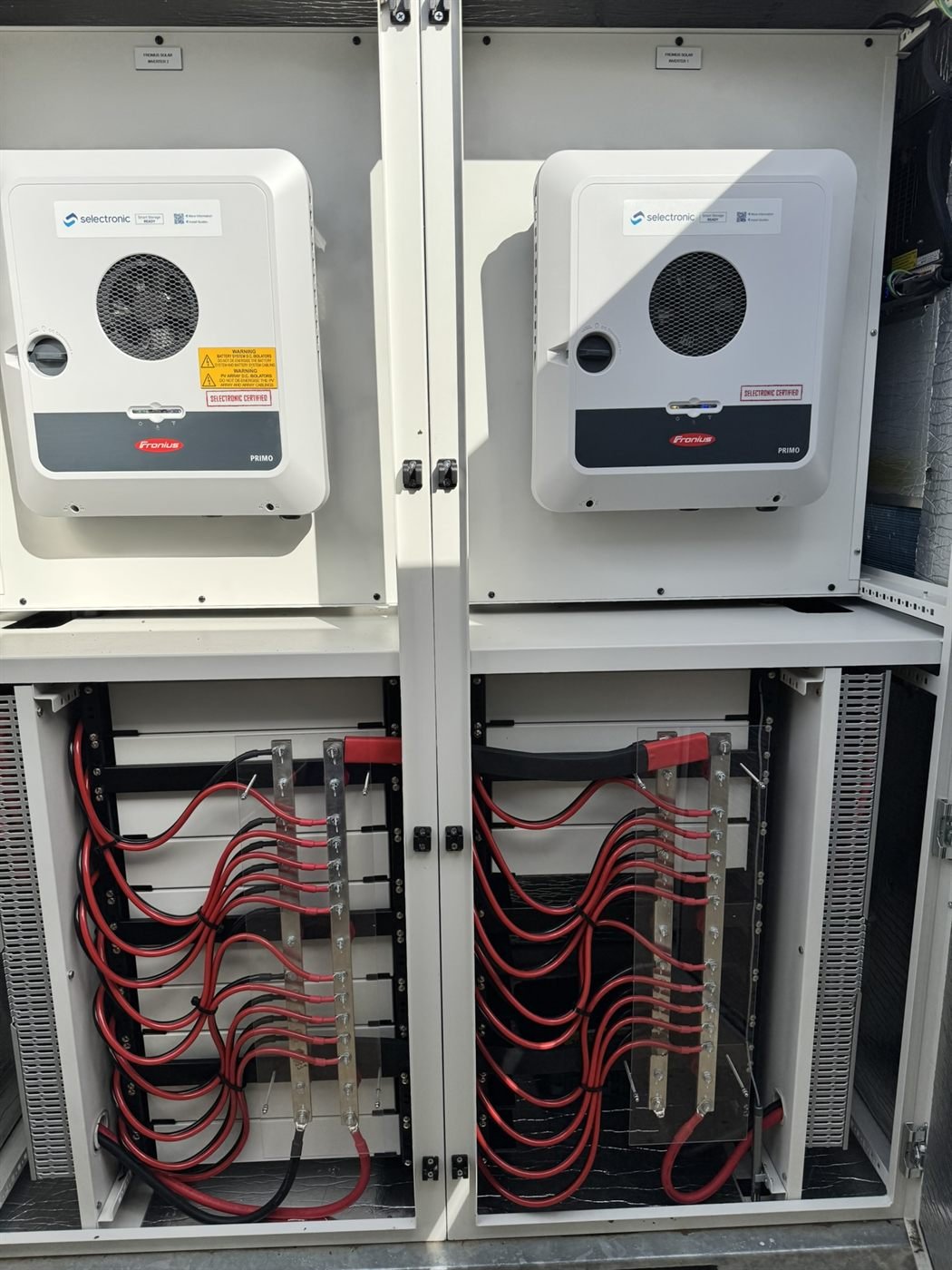 Fronius Primo inverters above a battery enclosure with bus-bar wiring