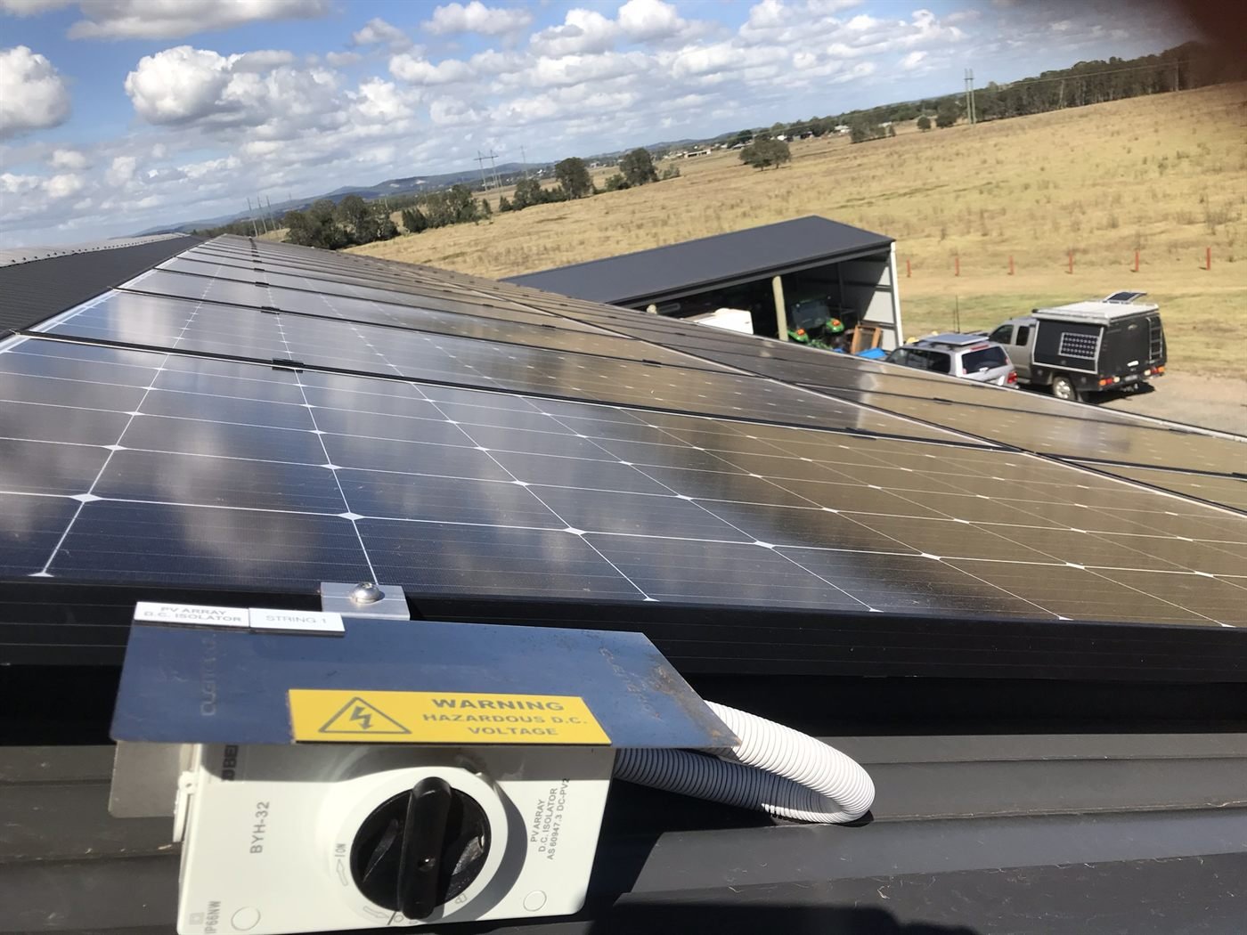 Rooftop solar panels on a rural farm shed with farmland behind
