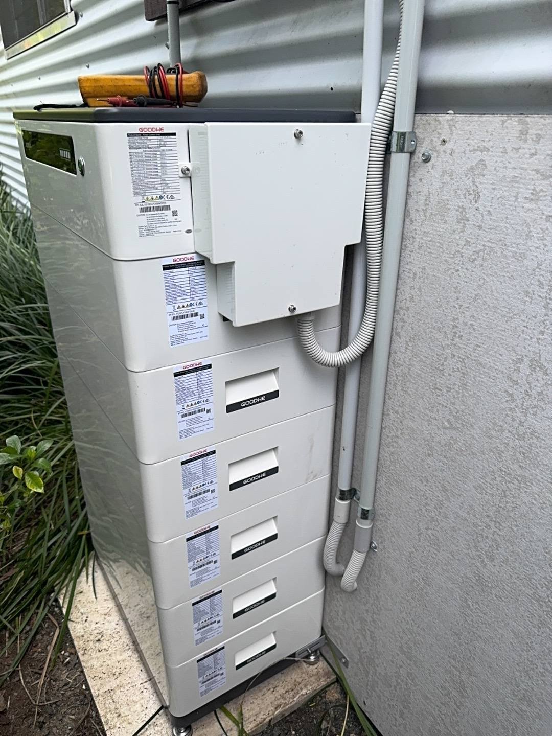 Stacked GoodWe home battery installed outdoors beside a shed wall, Stroud NSW